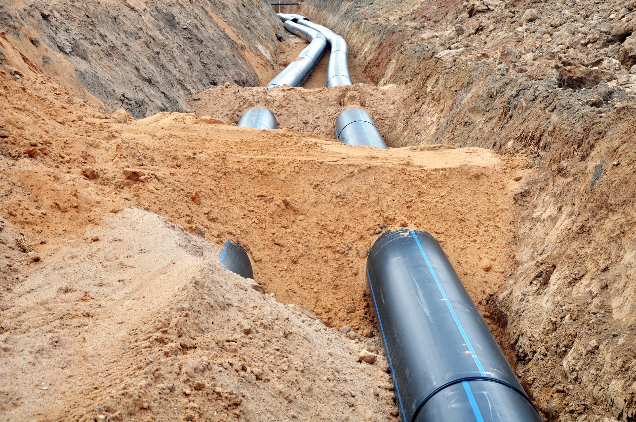 Browne Group - Large black pipes being installed in a trench, surrounded by dirt and sand at a construction site.