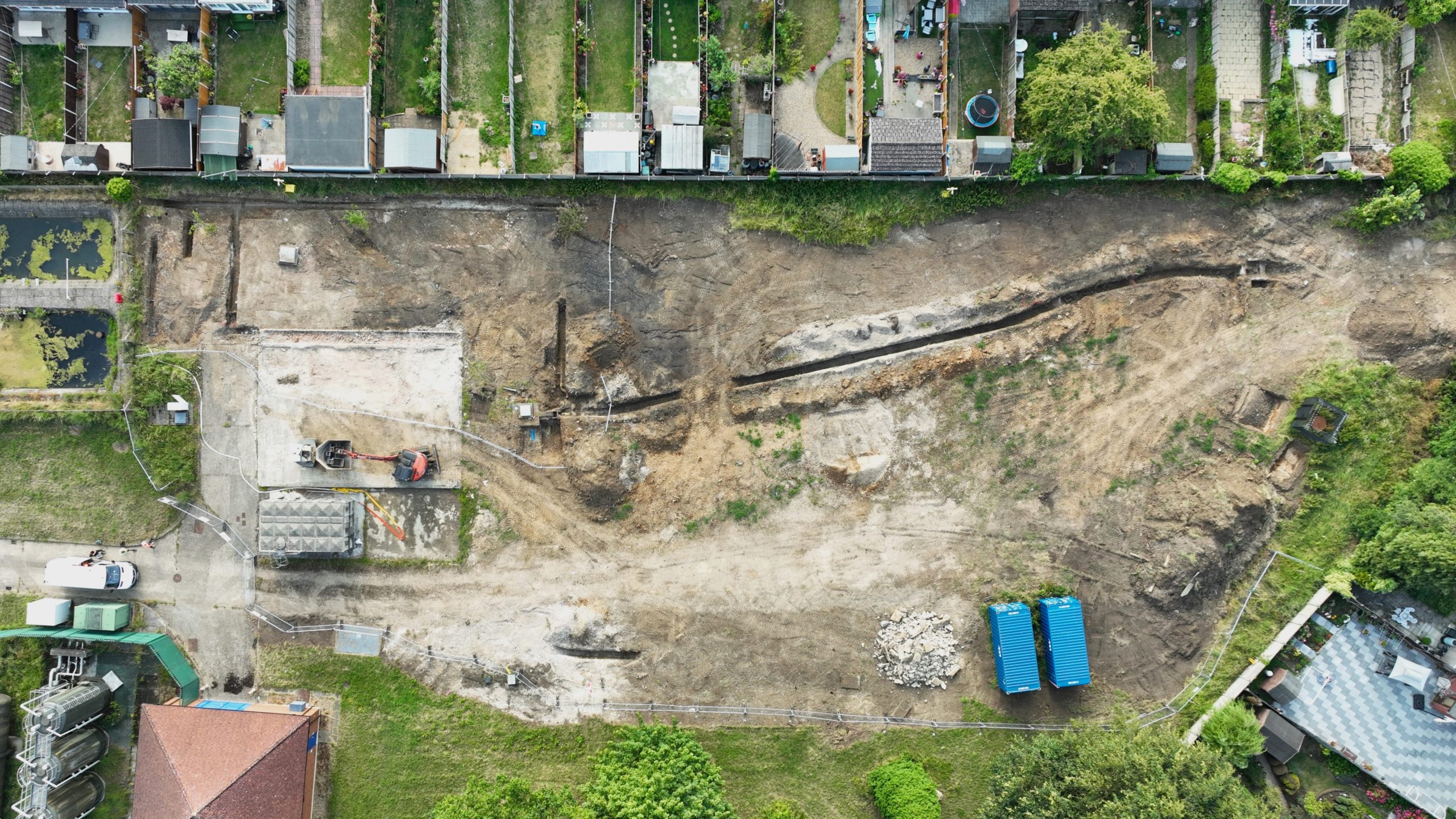 Browne Group - Aerial view of a construction site with machinery, dirt paths, and nearby houses and gardens.