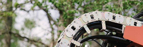 Browne Group - Close-up of an industrial cable carrier with trees and greenery blurred in the background.