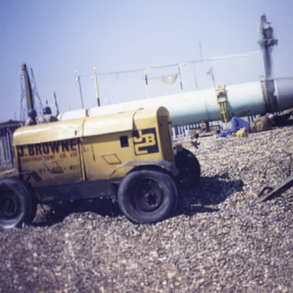 Browne Group - A yellow industrial machine on rocky ground, with a large pipe and workers in the background.