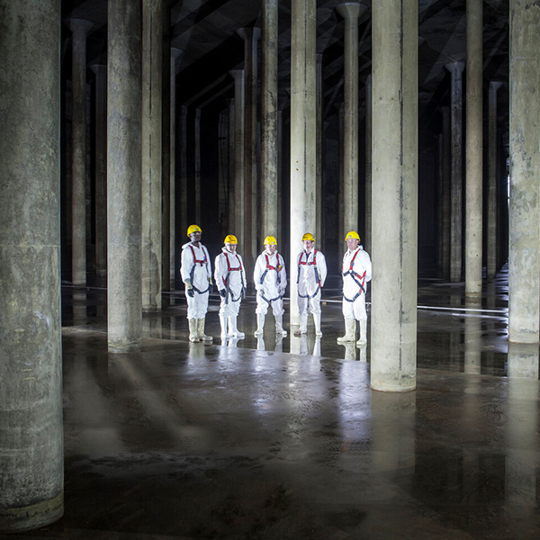 Browne Group - Five people in white protective suits and yellow helmets stand among large concrete columns in a dimly lit space.