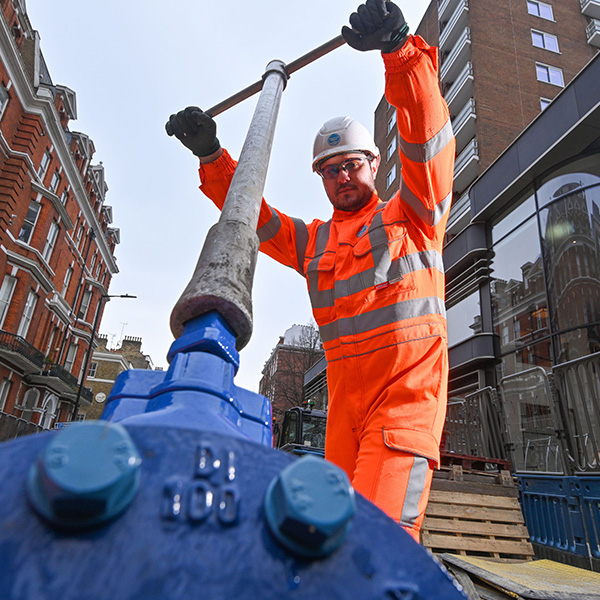 Browne Group - Worker in orange safety gear and helmet operates a large industrial valve on a city street.