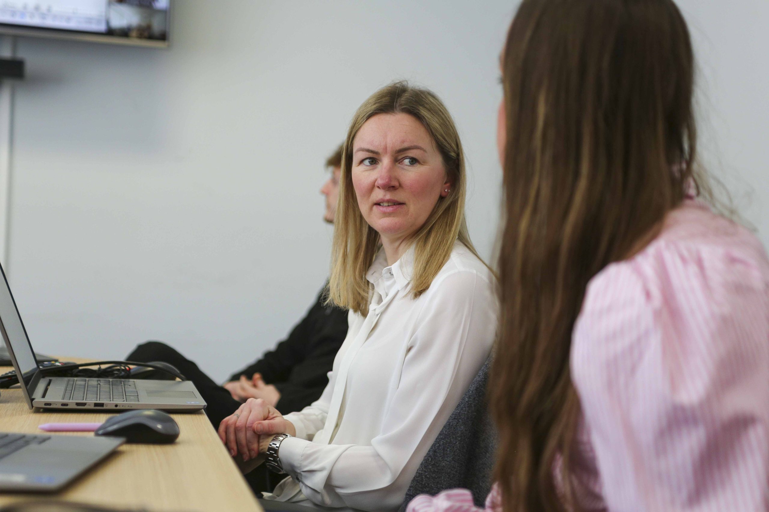 Browne Group - A woman in a white blouse talks to a colleague at a meeting table with laptops.
