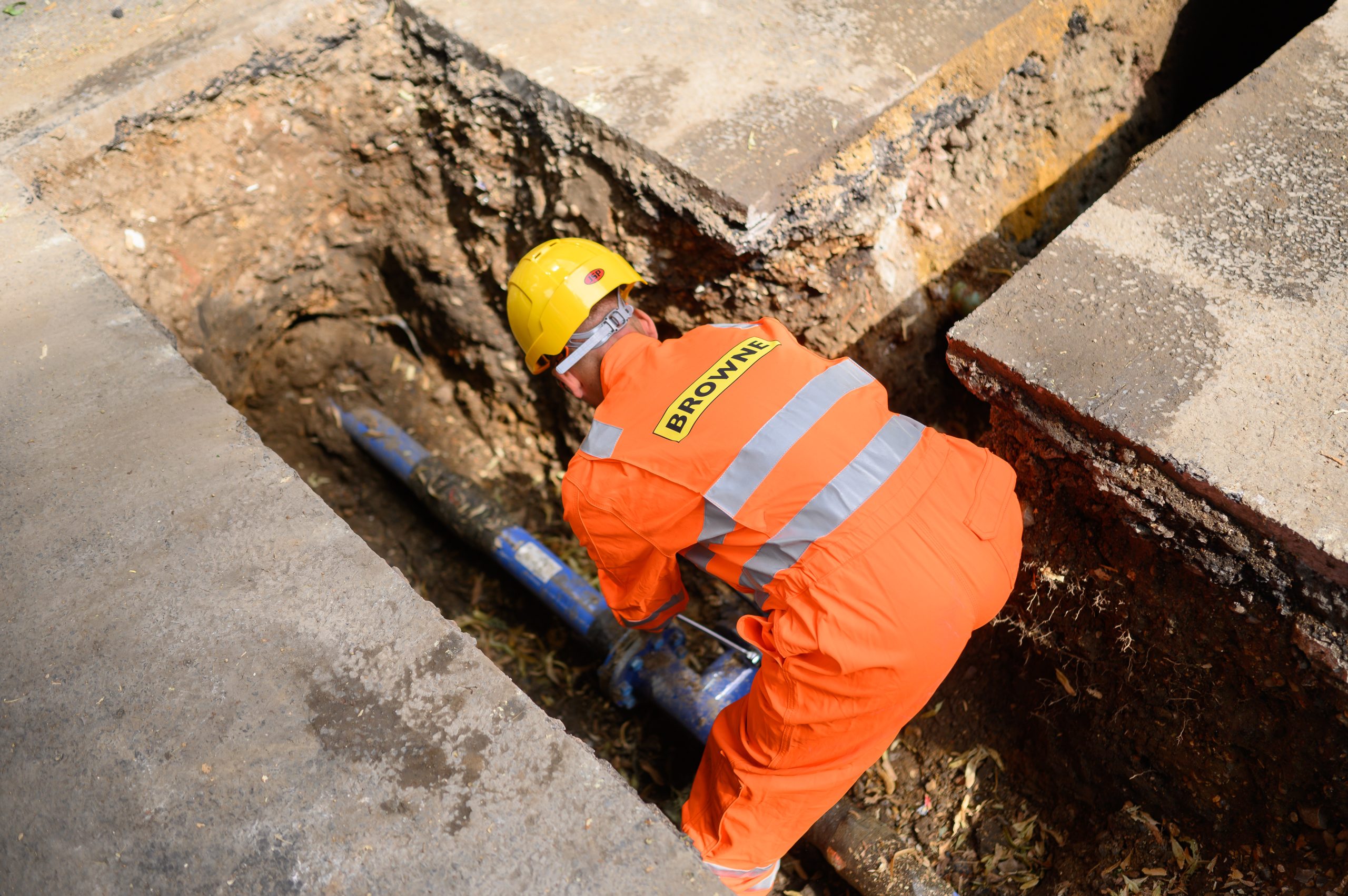 Browne Group - A worker in orange safety gear repairs a pipe in a deep trench at a construction site.
