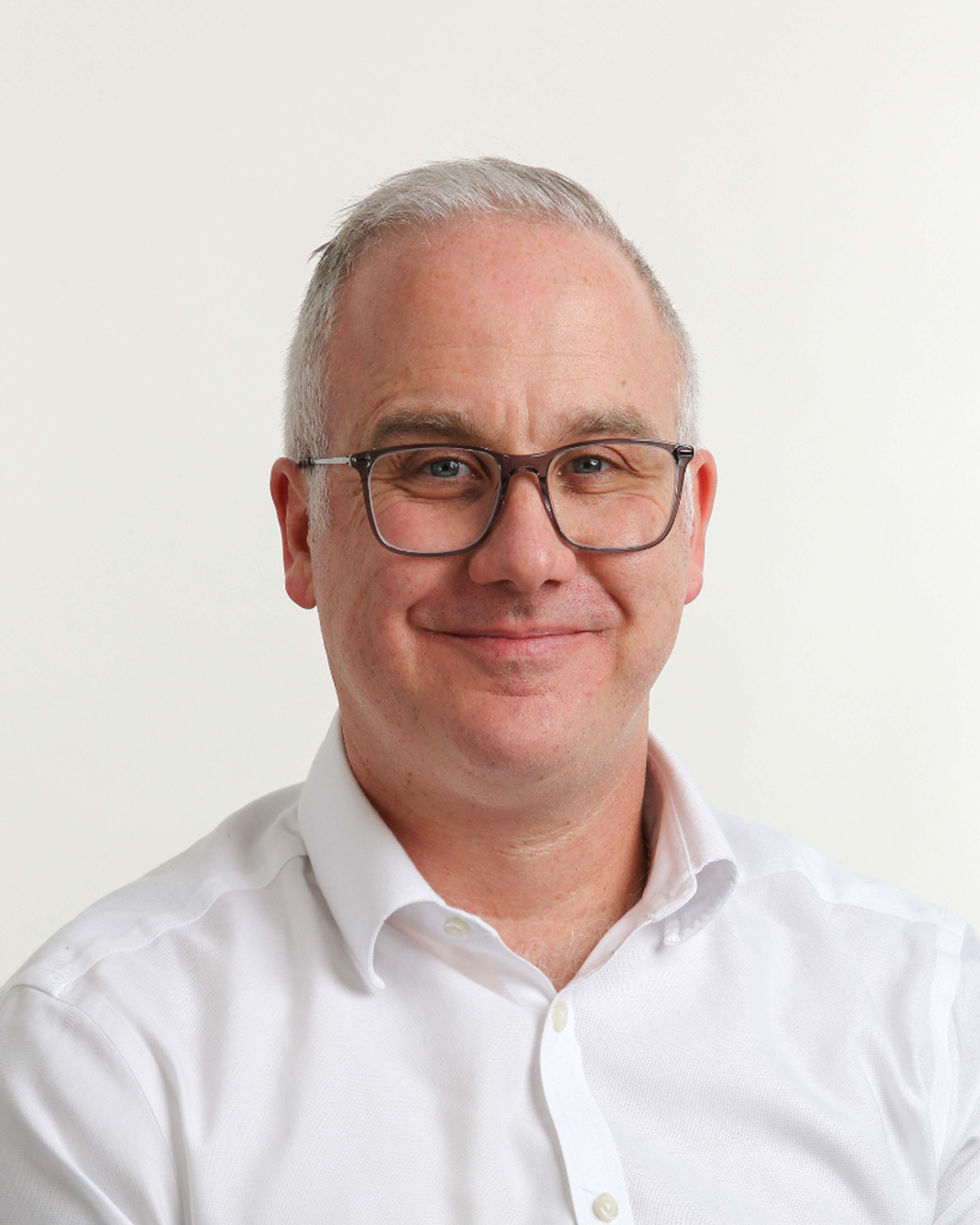 Browne Group - Smiling man with glasses and short gray hair wearing a white shirt against a plain light background.