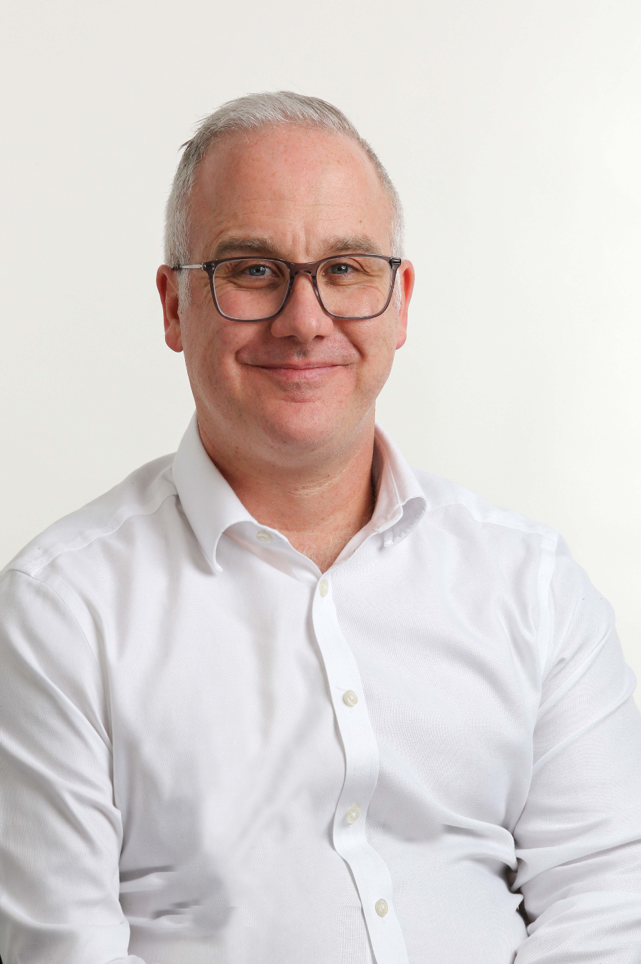 Browne Group - Smiling man with glasses and short gray hair wearing a white shirt, posing against a plain background.