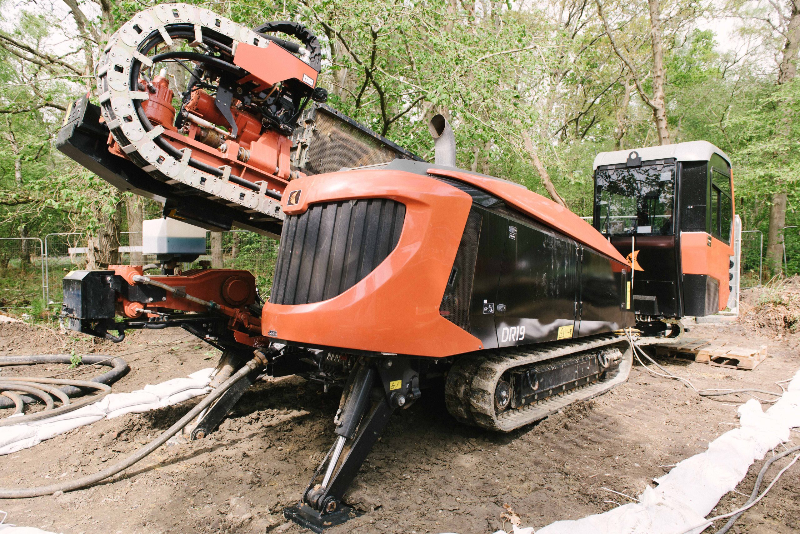 Browne Group - A large orange and black trenching machine parked on dirt in a wooded area.