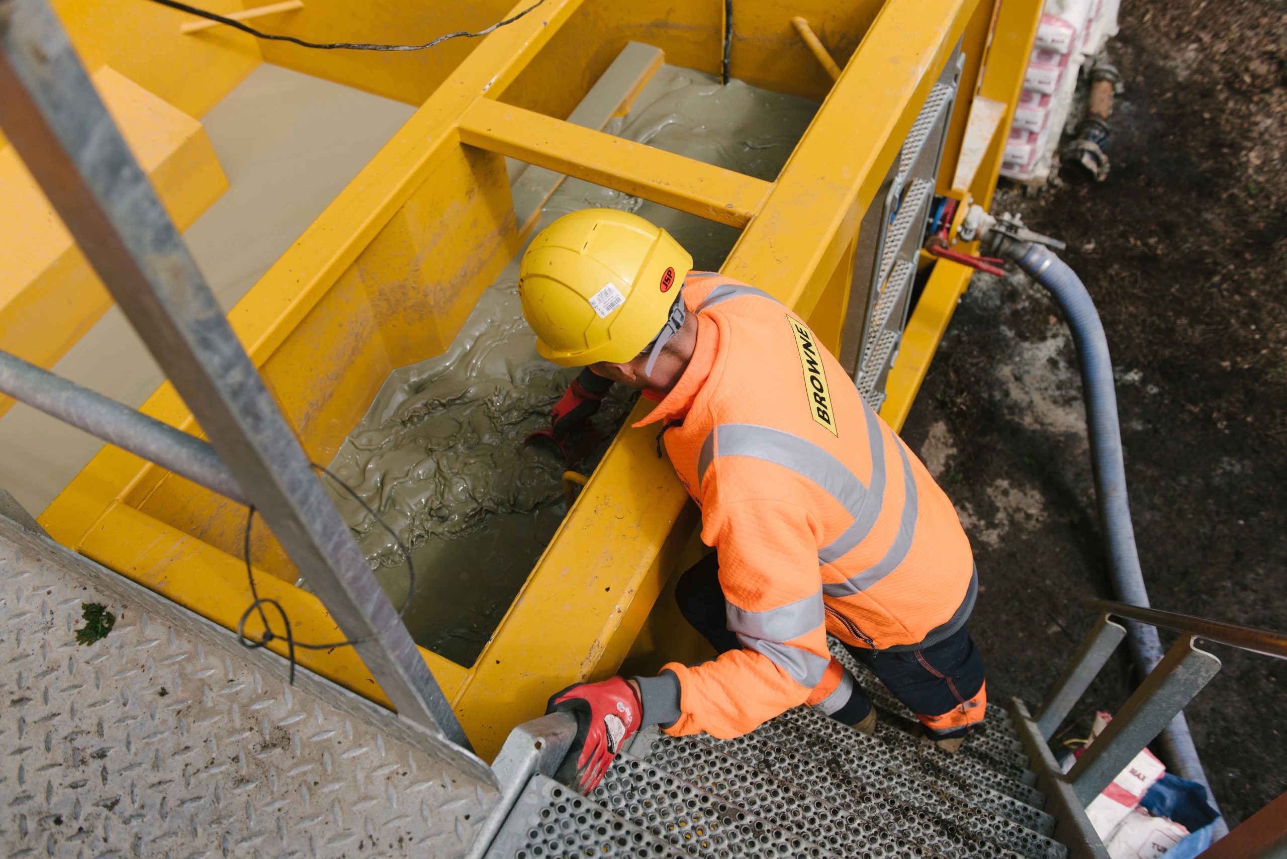 Browne Group - A construction worker in safety gear leans over a yellow tank filled with liquid concrete.