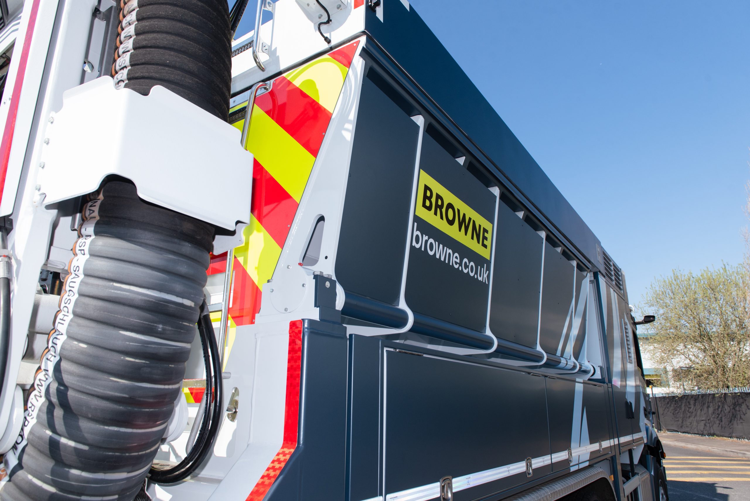 Browne Group - Close-up of a Browne company utility vehicle with hoses and warning stripes, parked under a clear blue sky.
