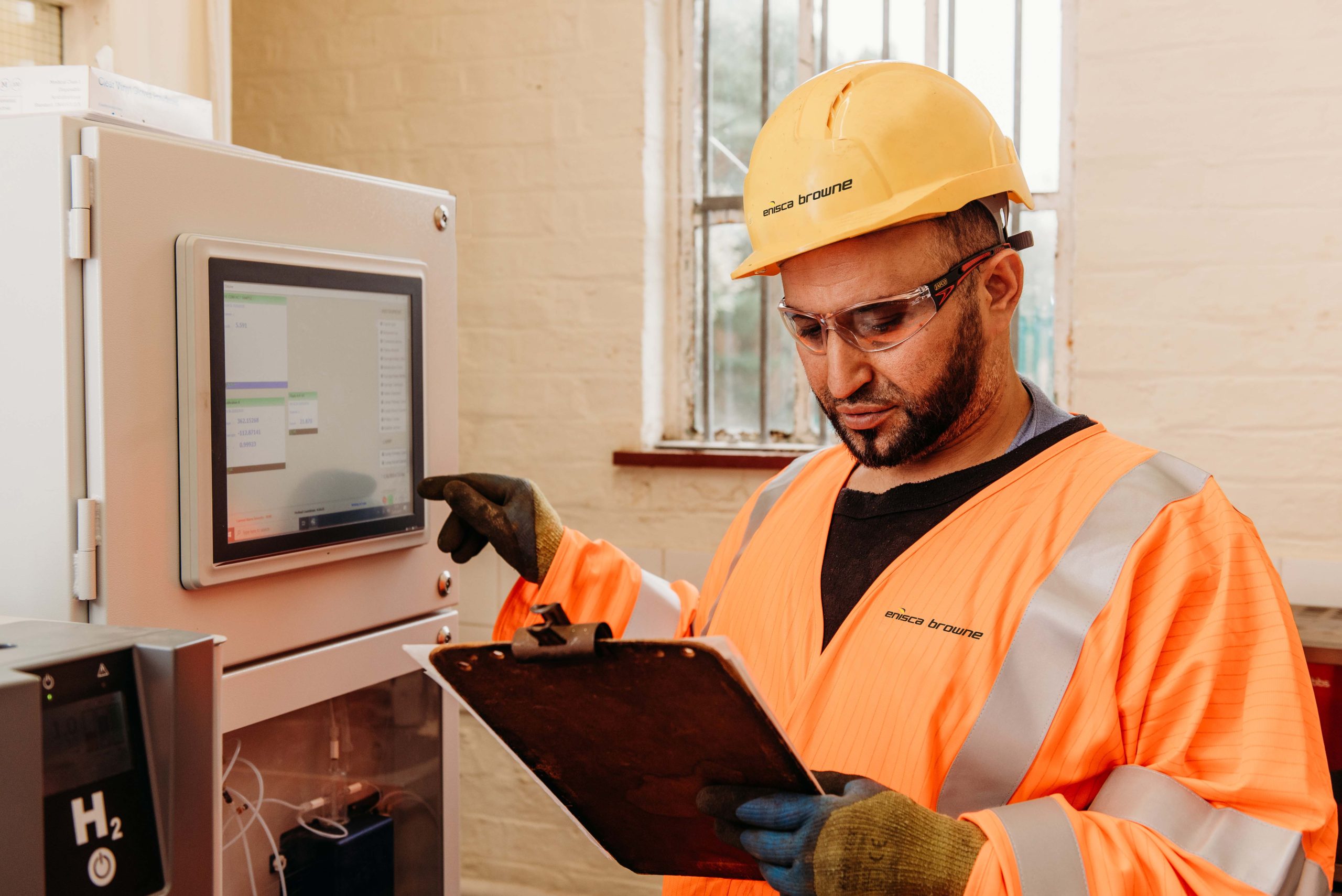 Browne Group - A worker in safety gear uses a touchscreen and holds a clipboard in an industrial setting.