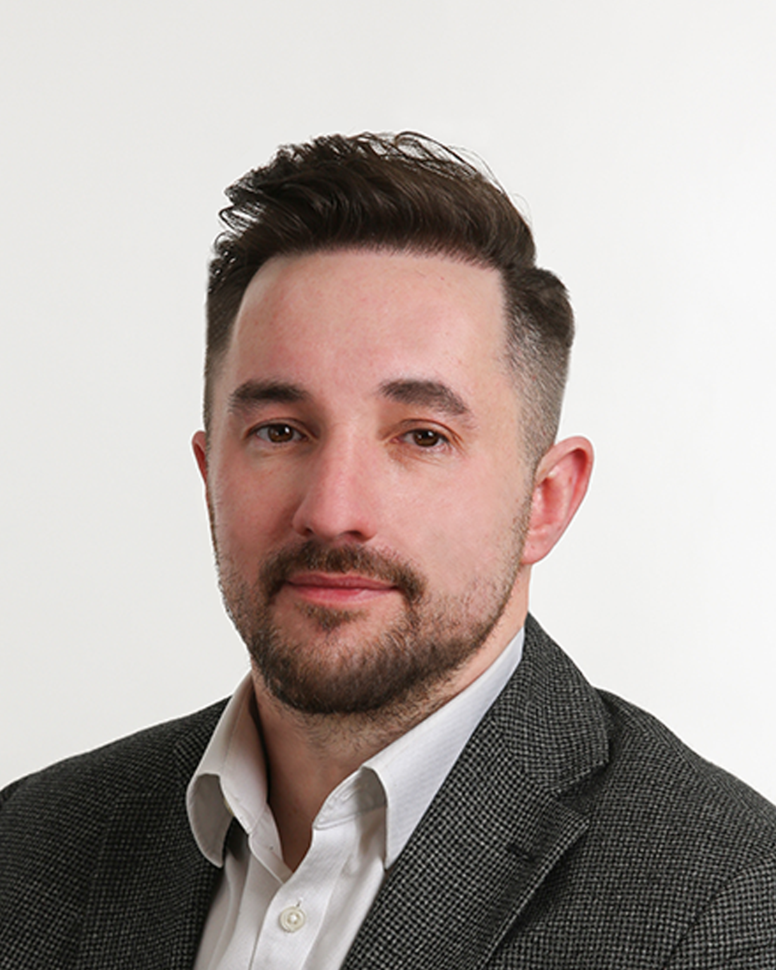 Browne Group - A man with short brown hair and a beard, wearing a grey blazer and white shirt, poses against a white background.