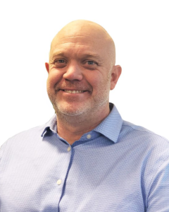 Browne Group - Smiling bald man with a trimmed beard wearing a light blue collared shirt, posed against a white background.