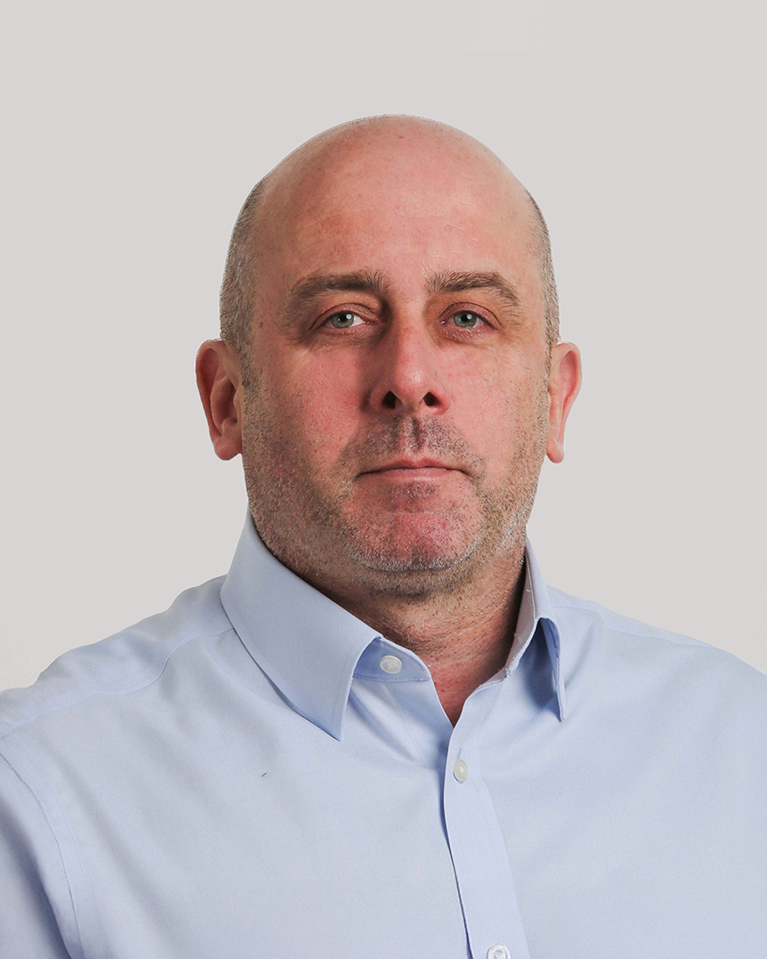 Browne Group - A man with a bald head and light stubble wearing a light blue collared shirt against a plain background.