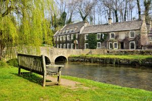 Browne Group - A wooden bench facing a stone bridge and a historic stone building beside a stream.