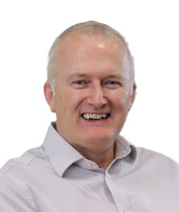 Browne Group - Smiling middle-aged man with short gray hair wearing a light checkered shirt, on a white background.