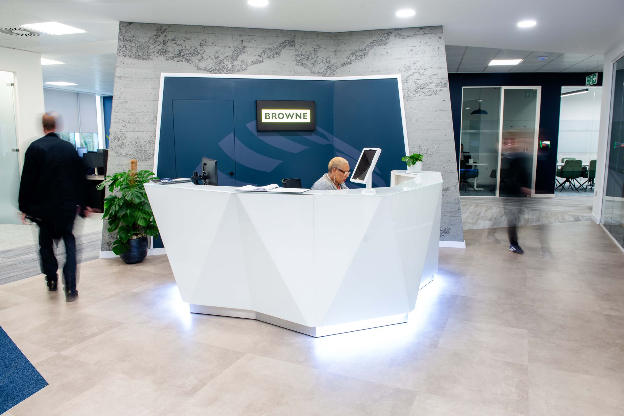 Browne Group - A receptionist sits at a modern white desk in an office lobby with people walking by and a sign that reads 