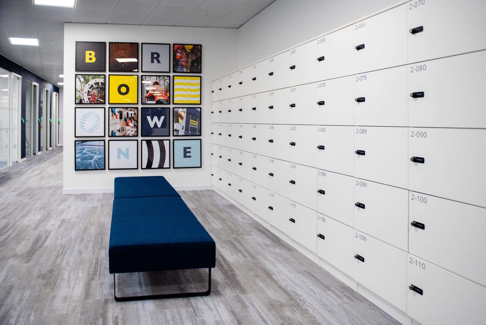 Browne Group - Modern hallway with blue bench, wall of white lockers, and colorful art squares spelling “BROWNE” on the wall.