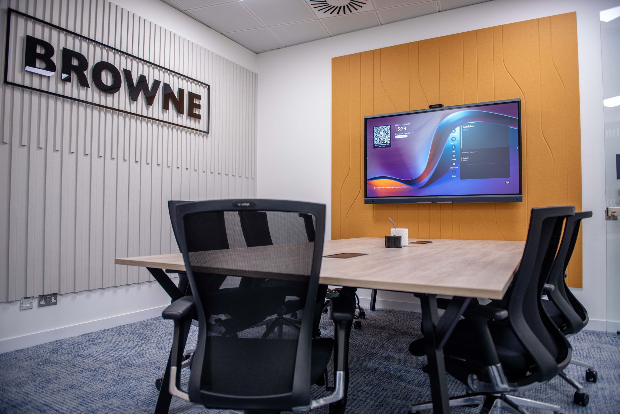 Browne Group - Modern meeting room with six chairs, a large screen on an orange wall, and a 