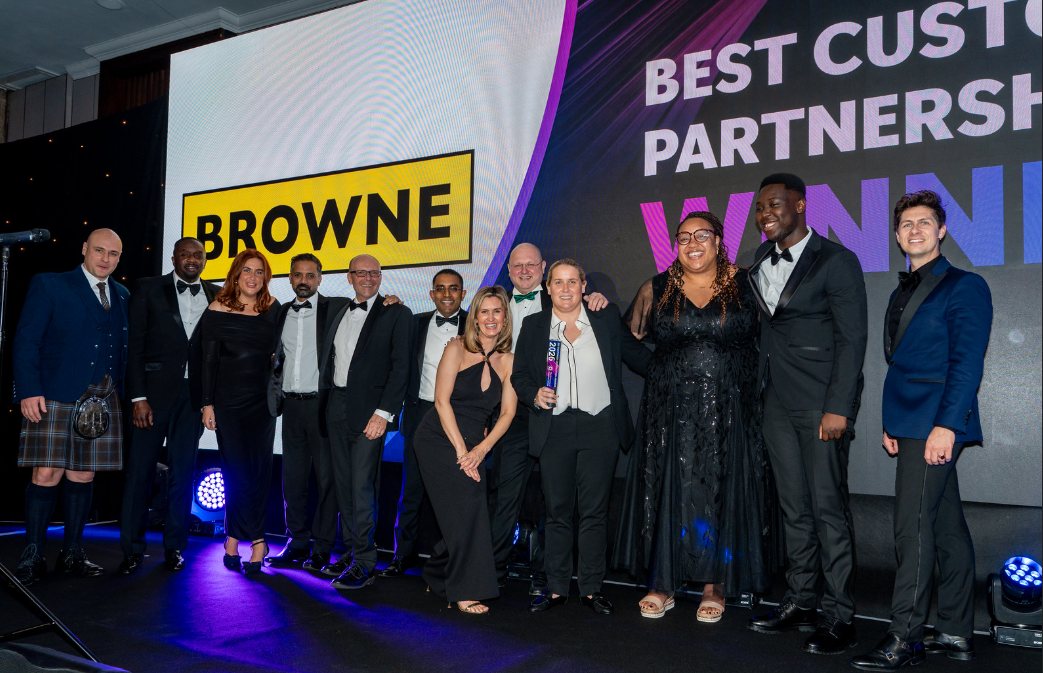 Browne Group - Thirteen people in formal attire pose on stage with a trophy under 