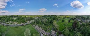 Browne Group - Aerial view of a village with stone houses, green trees, open fields, and a blue sky with scattered clouds.