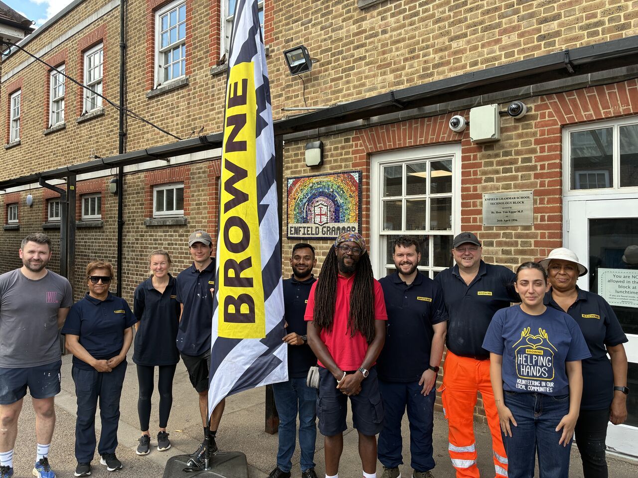 Browne Group - Group posing outside a brick building with a “Browne” flag, rainbow artwork, and Thames Water Raft Race banner.