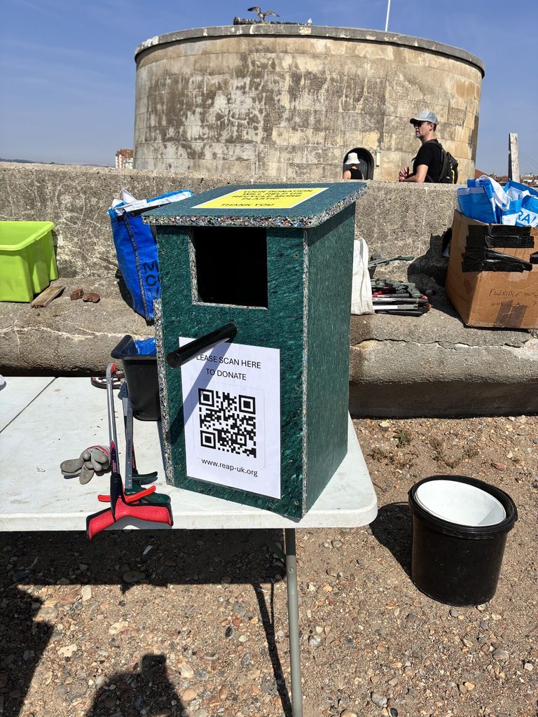Browne Group - Green donation box with QR code at Thames Water Raft Race, cleaning supplies and people visible in the background.