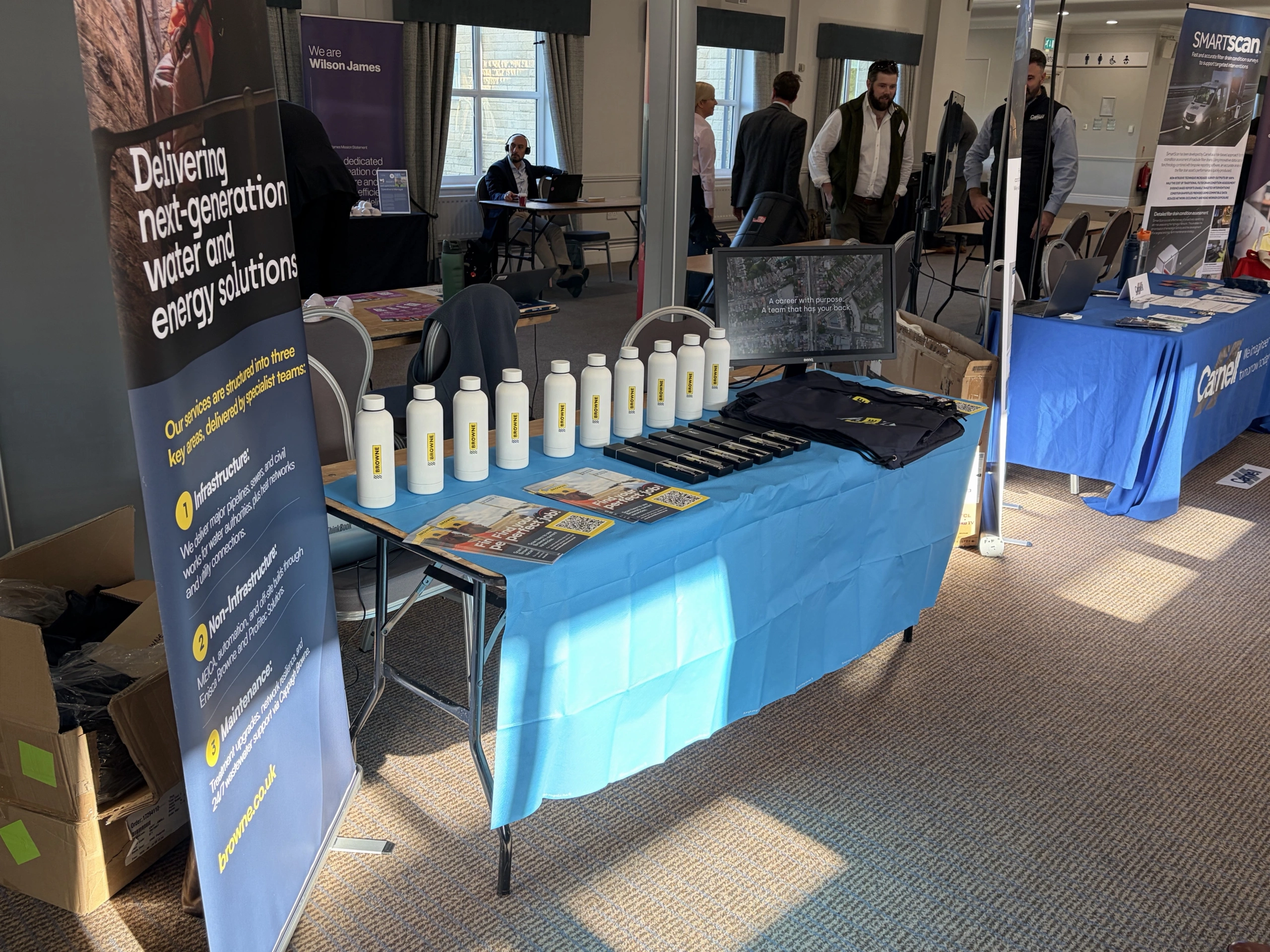 Browne Group - A corporate display table with branded white water bottles, informational brochures, and a computer monitor.
